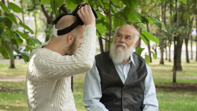 Grandson-with-grandfather-uses-a-virtual-reality-glasses-in-park