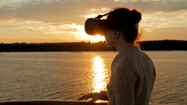 Frau-mit-virtual-Reality-Brille-auf-dem-Deck-des-Kreuzfahrtschiffes-bei-Sonnenuntergang