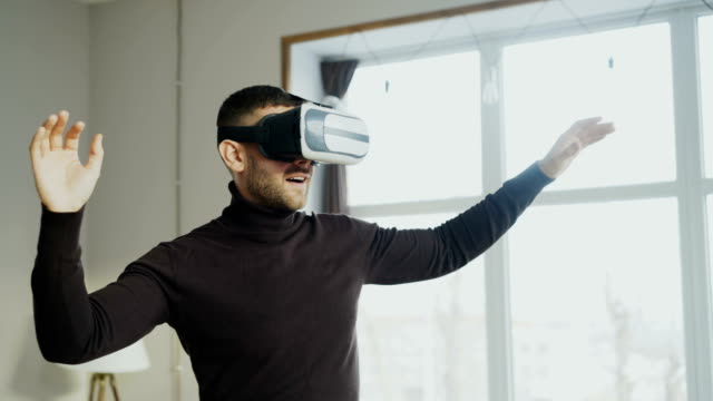 Excited-man-with-virtual-reality-headset-playing-360-video-game-at-home