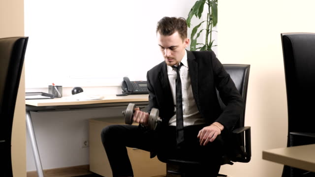 Work-out-in-the-office,-man-in-a-suit-does-an-exercise-for-the-biceps-while-sitting-in-the-office.-60-fps