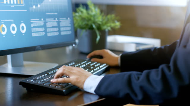 Close-up-Businessman's-Hands-Typing-on-Keyboard,-Desktop-Computer-Monitor-Shows-Infographics-with-Statistics.