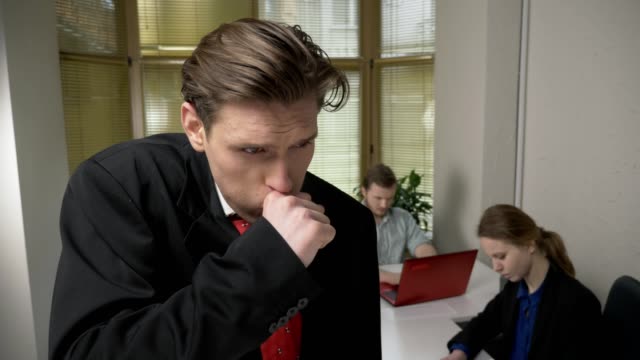Young-man-in-a-suit-is-coughing,-sick,-a-disease-concept.-Man-and-the-girl-in-the-background-are-working-in-the-office.-60-fps