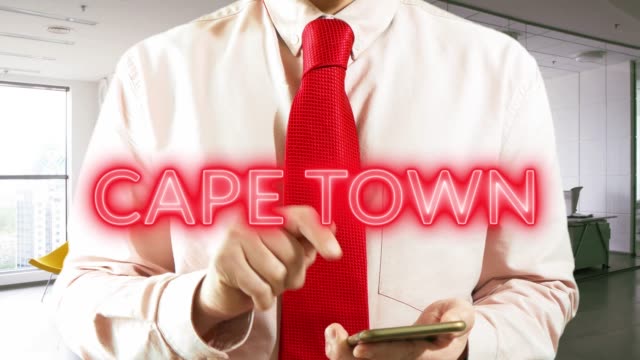 Cape-Town.-Businessman-operating-a-smart-device-chooses-а-city-on-light-background.-Concept:-business-trip,hologram,-technology,-augmented-reality,-future,-travel