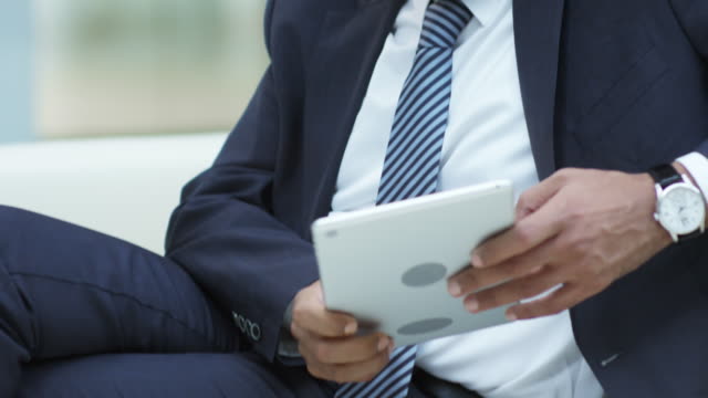 Hombre-de-negocios-sentado-en-sofá-y-mensajes-de-texto-en-tableta