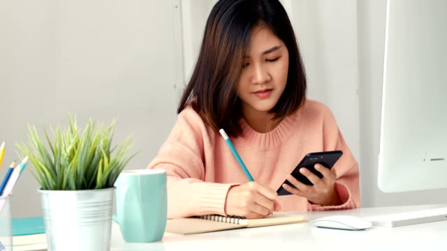 Jóvenes-mujeres-asiáticas-los-dueños-de-negocios-usando-la-aplicación-smartphone-y-tomar-notas-en-la-oficina.