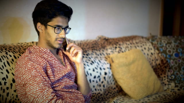 Handsome-Indian-Man-In-Glasses-Discussing-By-Phone-Business-Questions-Sitting-On-The-Sofa