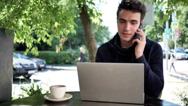 Mann-Reden-am-Telefon-während-der-Arbeit-am-Laptop-im-Cafe-Terrasse