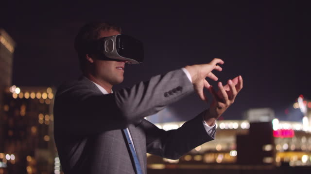 Young-business-man-wearing-VR-headset-at-night-creating-ball-with-hand-gestures