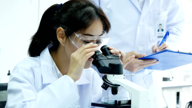 Mujer-científico-mirando-al-microscopio-con-asistencia.-Personas-con-médicos,-médico,-ciencia,-concepto-profesional-de-la-salud.-Resolución-de-4K.