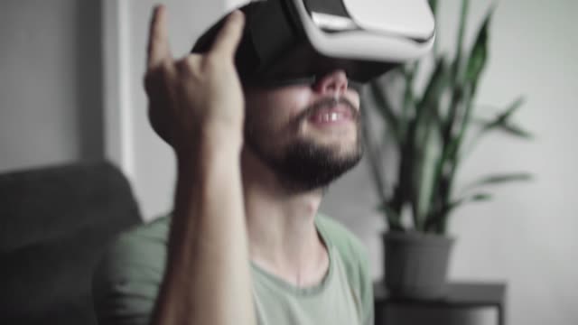 Junge-bärtige-Hipster-Mann-mit-seinem-VR-Kopfhörer-Anzeige-für-beobachten-360-Video-und-fühlt-sich,-als-er-auf-ein-Rock-Konzert,-beim-Sitzen-auf-dem-Sofa-zu-Hause-im-Wohnzimmer-ist.-VR-Technologie.