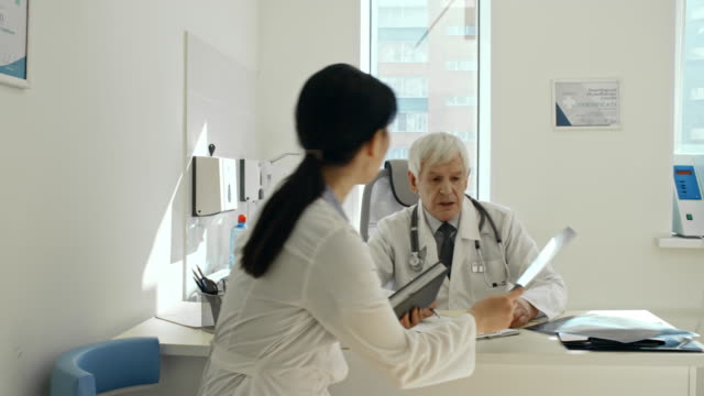 Weibliche-asiatische-Arzt-Röntgen-mit-älteren-Kollegen-diskutieren