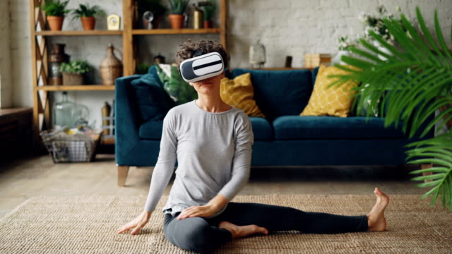 Lächelndes-Mädchen-in-virtual-Reality-Brille-sitzt-Training-zu-Hause-Erdgeschoss-dehnen,-Beine-und-Körper-und-genießen-AR.-gesunden-Lebensstil-und-Vr-Simulation-Konzept.