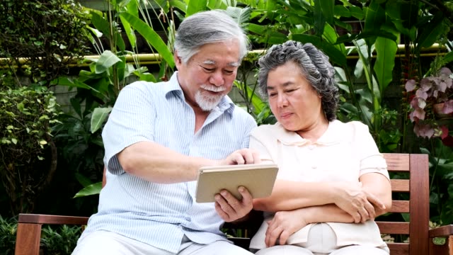 Senior-couple-sitting-and-using-tablet-together-in-home-garden.