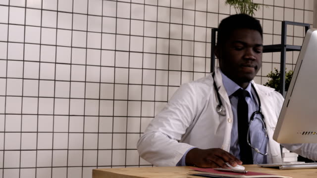 Doctor-masculino-africano-entrando-sentado-en-el-escritorio-y-el-inicio-de-trabajo