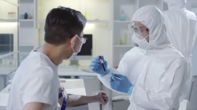 Doctor-in-Protective-Gear-Showing-Blood-Sample-to-Patient