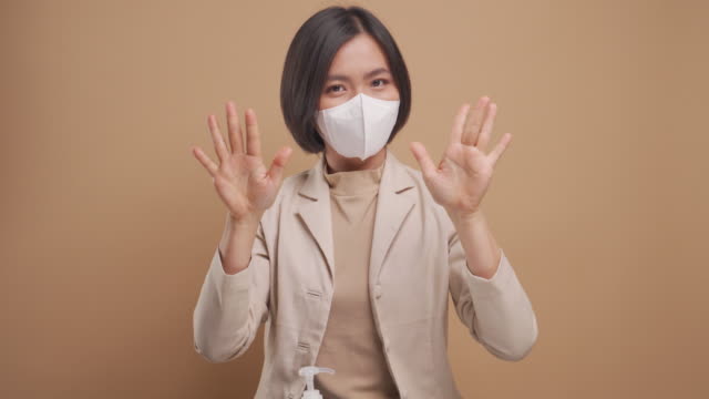 Una-mujer-de-negocios-asiática-que-usa-máscara-de-higiene-usó-gel-desinfectante-para-lavarse-las-manos-aislado-sobre-fondo-beige.-Vídeo-4K