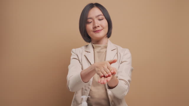 Asiatische-Geschäftsfrau-setzen-Hand-desinfektionsmittel-auf-Hände-für-waschen-ihre-Hände-isoliert-über-beige-Hintergrund.-4K-Video