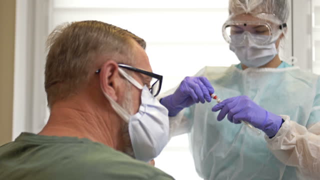 Krankenhausmitarbeiter-in-einem-Schutzanzug-nimmt-einen-Tupfer-von-einem-älteren-Patienten-für-Coronavirus