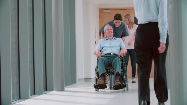 Krankenschwester-mit-älteren-Patienten-im-Rollstuhl-Schieben-an-Korridor