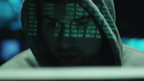 Männliche-Hacker-arbeiten-mit-einem-Computer-und-grüne-Code-Zeichen-Ausdruck-auf-seinem-Gesicht-im-dunklen-Büro-Zimmer.