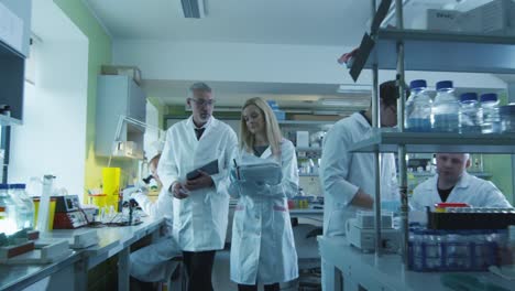 Senior-and-female-scientists-with-papers-and-tablet-are-walking-and-having-a-conversation-in-a-laboratory.