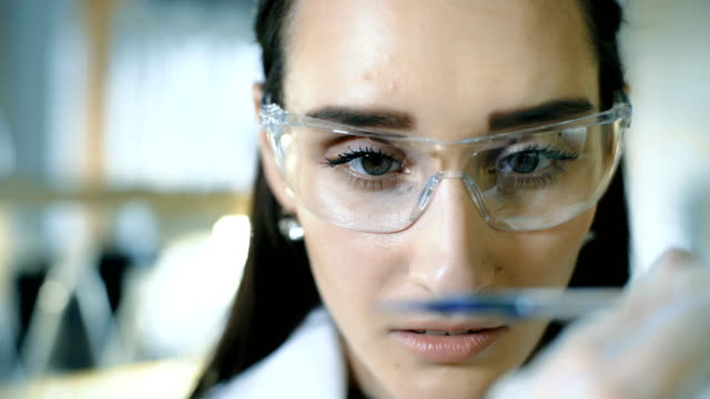 Young-female-scientist-holding-test-tube-with-liquid-sample-making-research-in-clinical-laboratory