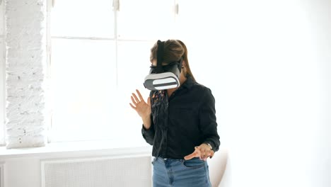 Frau-in-VR-Kopfhörer-nachschlagen-und-versuchen,-Objekte-in-der-virtuellen-Realität-in-weißen-Raum-drinnen-berühren