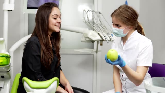 Dentista-mujer-joven-con-manzana-verde-al-paciente-sano-y-feliz-después-de-los-procedimientos