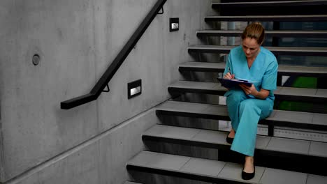 Nurse-sitting-on-steps-and-writing-on-clipboard