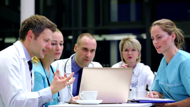 Equipo-de-médicos-discutiendo-sobre-laptop-en-la-sala-de-conferencias