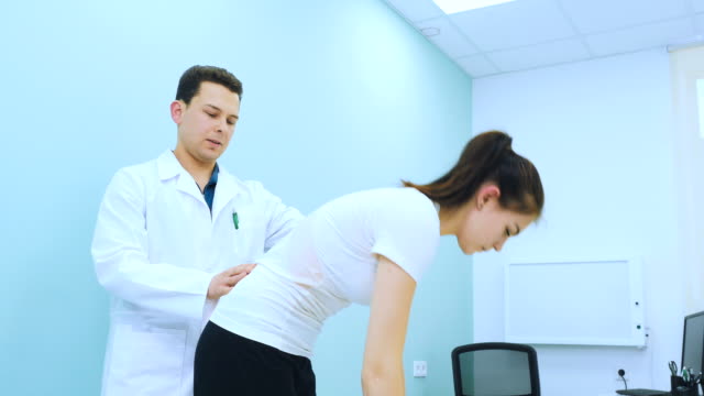 Ein-junger-Arzt-untersucht-den-Rücken-des-Mädchens-in-Rehabilitationskabinett