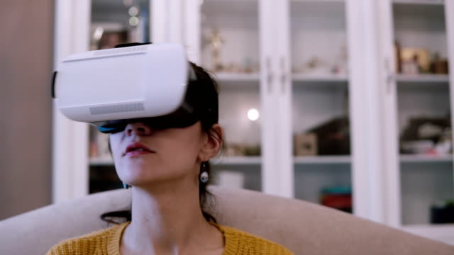 Vista-cercana-de-joven-mujer-en-gafas-de-realidad-virtual-sentado-en-el-sofá-en-casa.-Mujer-mirando-a-su-alrededor-en-VR-casco-con-auriculares