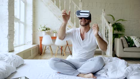Fröhliche-junge-Mann-tragen-virtual-Reality-Kopfhörer-360-VR-video-Film-sitzen-im-Bett-zu-Hause
