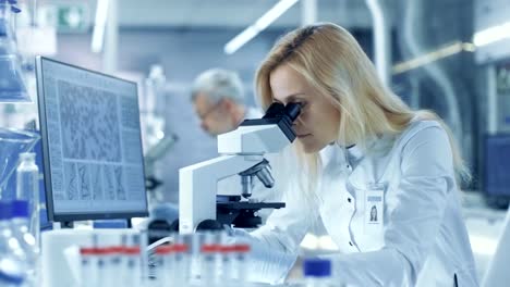 Female-Research-Scientist-Looks-at-Biological-Samples-Under-Microscope,-Types-Results-into-Computer.-She-and-Her-Colleagues-Work-in-a-Big-Modern-Laboratory/-Medical-Centre.