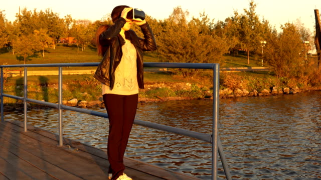 Junge-Frau-mit-einer-virtual-Reality-Brille-auf-der-Mole-bei-Sonnenuntergang