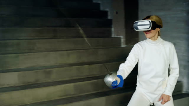 Concentrated-fencer-woman-using-virtual-reality-headset-for-play-fencing-training-simulator-game-indoors