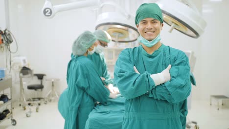 Retrato-de-cirujano-masculina-caucásica-usar-completo-quirúrgico-friega-cámara-sonriente-con-los-médicos-del-equipo-operando-en-paciente-en-quirófano-en-el-hospital.