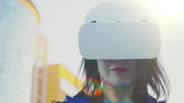 Mujer-joven-con-gafas-VR,-auriculares,-jugar-juegos-virtuales-y-ver-vídeos-al-aire-libre-contra-el-fondo-de-un-edificio-de-cristal