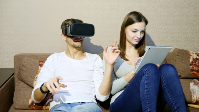 Hombre-usando-dispositivo-de-realidad-virtual-mientras-la-mujer-escribiendo-en-tableta-digital