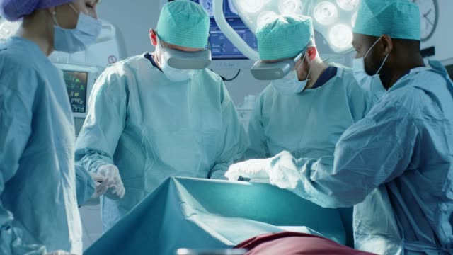 Surgeons-Wearing-Virtual-Reality-Glasses-to-Perform-State-of-the-Art-Surgery-in-Technologically-Advanced-Hospital.-Doctors-and-Assistants-Working-in-Operating-Room.