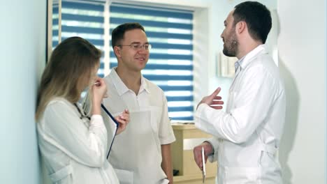 Male-doctor-holding-tablet-talking-to-two-others-doctors-in-the-hospital-hall