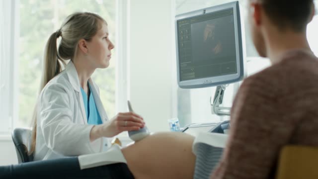 Im-Krankenhaus,-schwangere-Frau-im-Bett-liegend,-Geburtshelfer-drückt-Tasten-auf-eine-Schalttafel-und-beginnt-Ultraschall-/-Ultraschall-Verfahren.-Mann-unterstützt-seine-Frau.