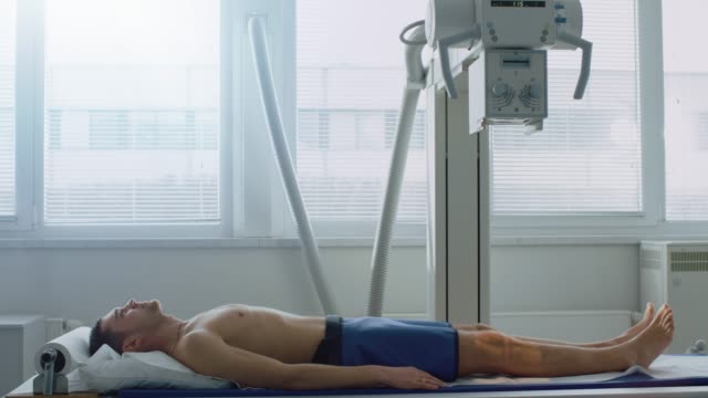 Im-Krankenhaus-Man-sitzt-auf-einem-Bett-warten-Röntgengerät-um-sein-Bein-nach-Verletzungen-zu-suchen.-Suche-nach-Frakturen,-gebrochene-Gliedmaßen,-Krebs-oder-Tumor.-Moderne-Krankenhaus-mit-technologisch-fortschrittlichen-medizinischen-Geräten.
