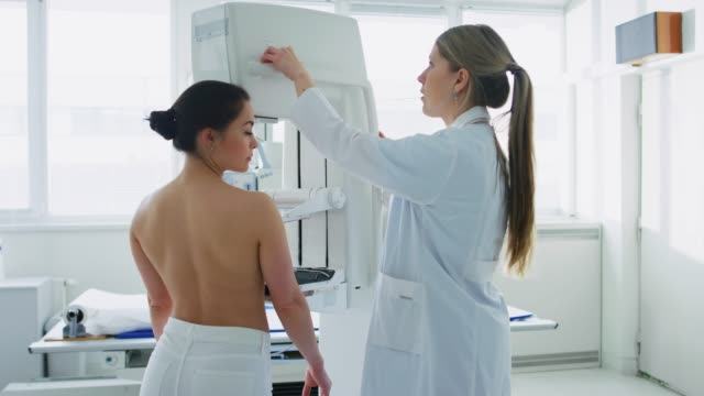 In-der-Klinik,-Mammographie-Technologe-/-Arzt-Mammographie-Maschine-für-eine-Patientin-passt.-Freundlicher-Arzt-erklärt-die-Bedeutung-der-Prävention-von-Brustkrebs.-Moderne-technologisch-Klinik-mit-Fachärzten.