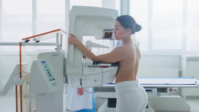 Im-Krankenhaus,-Seite-Ansicht-Schuss-oben-ohne-weibliche-Patienten-unterziehen-Mammographie-Screening-Verfahren.-Gesunde-junge-Frau-hat-Krebs-vorbeugende-Mammographie-Scan.-Moderne-Krankenhaus-mit-Hightech-Maschinen.