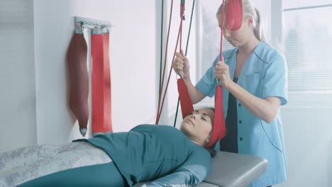Physiotherapist-Assists-Female-Patient-with-Trauma,-Undergoing-Rehabilitative-Physiotherapy-on-a-Special-Suspension-Rope-System.-Relieving-Neck,-Back,-Head-Pain.-Modern-Clinic-Using-Most-Advanced-Rehabilitating-Procedures.