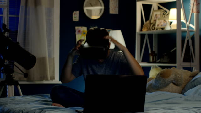 Boy-using-VR-glasses-and-laptop-on-bed