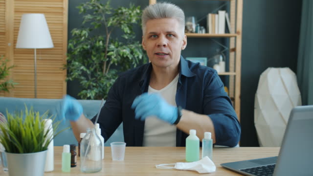 Portrait-of-adult-man-making-hand-sanitizer-at-home-holding-bottles-looking-at-camera-talking