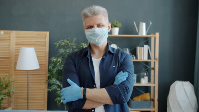 Portrait-of-mature-guy-in-face-mask-and-gloves-standing-in-apartment-during-pandemic