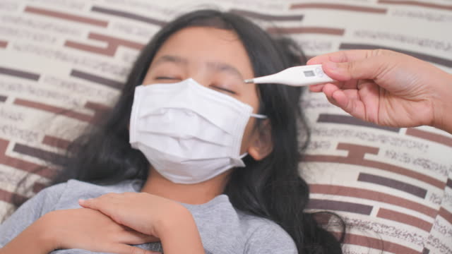 Una-niña-asiática-enferma-en-casa-y-tosiendo.-La-madre-midió-la-fiebre-de-la-hija-con-mercurio.